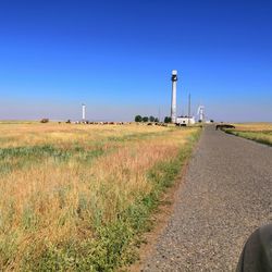 Road amidst field against clear blue sky