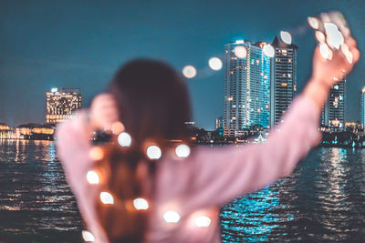 Rear view of man photographing illuminated cityscape against sky