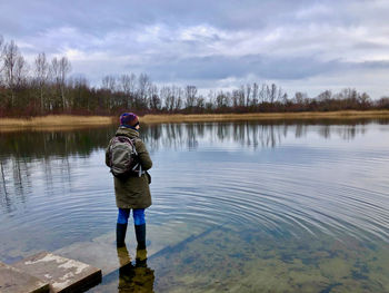 Rear view of woman standing by lake against sky