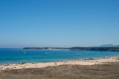 People on beach against clear blue sky