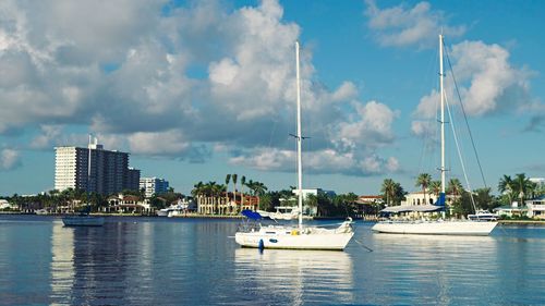 Sailboats moored in harbor by buildings against sky