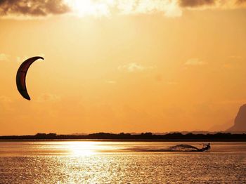 Silhouette person kiteboarding in sea against orange sky during sunset