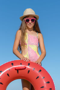 Portrait of a teenage girl in sunglasses and a hat with an inflatable ring against the sky. 