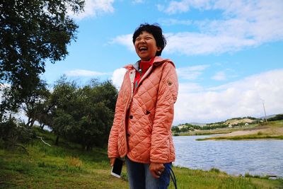 Cheerful woman laughing at riverbank against sky