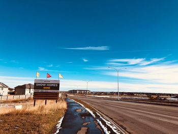 Road sign by street against blue sky