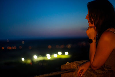 Side view of woman sitting by sea against sky at night