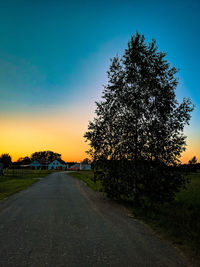 Road amidst trees on field against sky at sunset