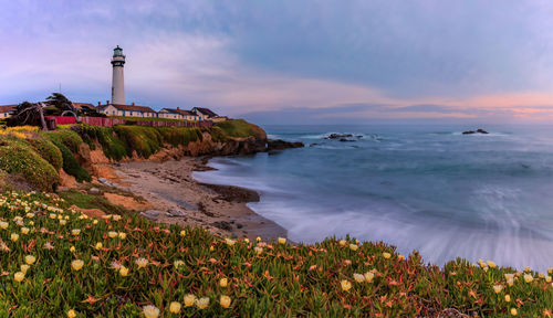 Lighthouse by sea against sky during sunset