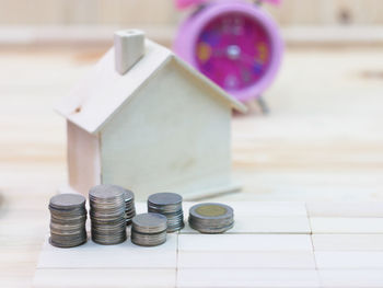 Close-up of coins in cup and model house by alarm clock on table