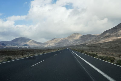 Empty road by mountains against sky