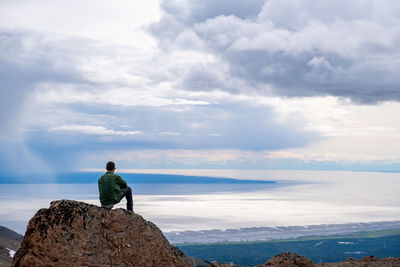 People sitting on rock by sea against sky