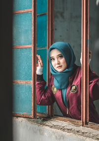 Portrait of young woman standing against window