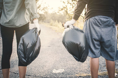 Midsection of people holding garbage bags while standing on road