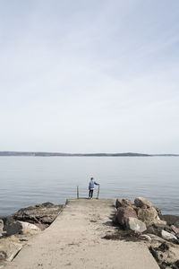 Men standing on rocks by sea against sky