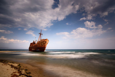 Abandoned boat on beach against sky during sunset