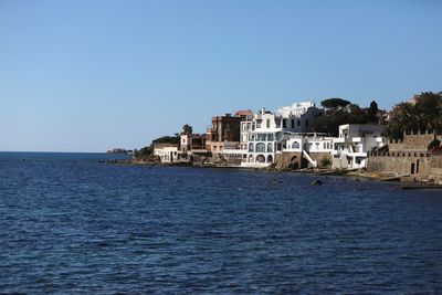 Buildings by sea against clear blue sky