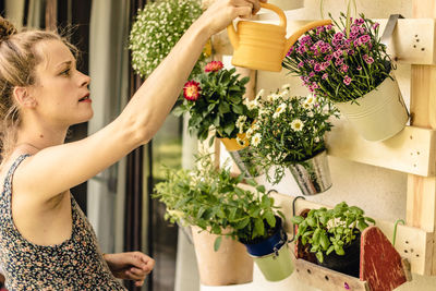 Beautiful young woman watering her potted plants on the balcony