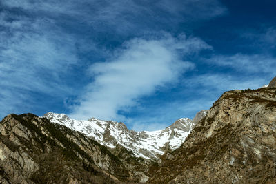 Low angle view of snowcapped mountains against blue sky