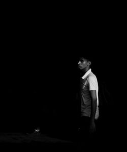 Side view of young man looking away while standing against black background