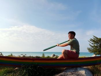 Man sitting on moored boat on land against sky