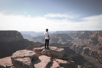 Rear view of man standing on rock against sky
