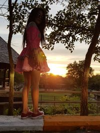 Full length of woman standing against trees during sunset