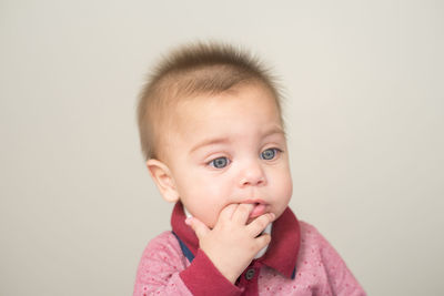 Cute boy with finger in mouth looking away against white background