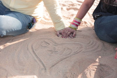 Low section of friends on sand at beach
