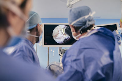 Professionals monitoring surgery on computer screen while standing in operating room