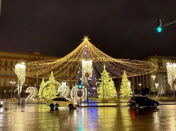 Illuminated ferris wheel in city against sky at night