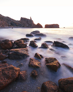 Scenic view of sea against clear sky with rocks above the water in a long exposure image