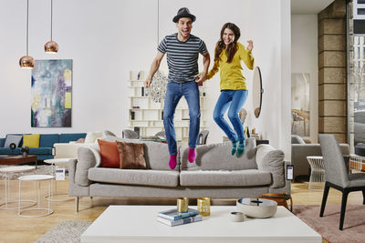 Couple in modern furniture store jumping on couch