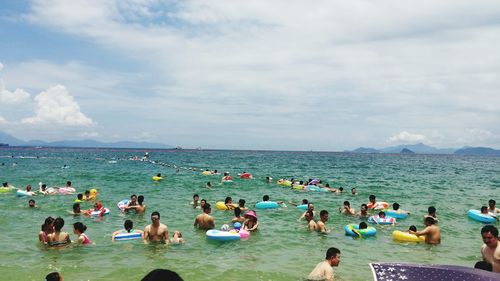 People swimming at sea against cloudy sky