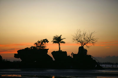 Silhouette rocks in sea against sky during sunset