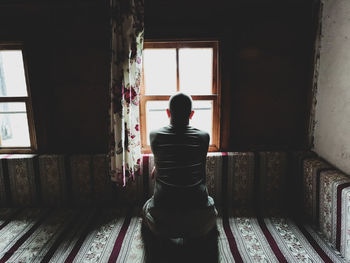 Rear view of man looking through window at home