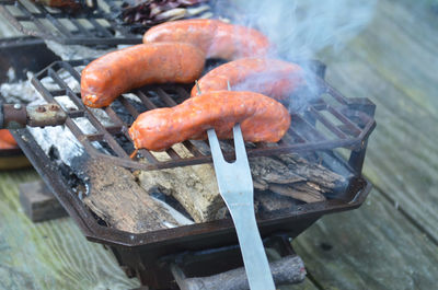 Hibachi tabletop grill on picnic table, flames, italian sausages, fork, smoky