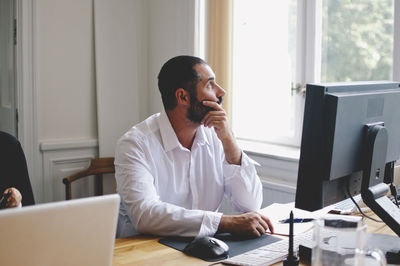 Thoughtful mature businessman sitting at table in creative office