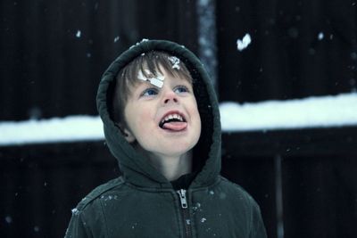 Close-up boy in warm clothing sticking out tongue outdoors