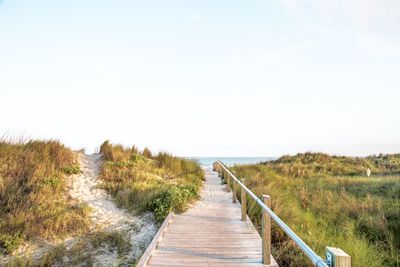 Boardwalk leading towards sea against sky at beach