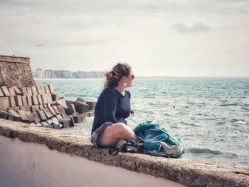 Side view of man sitting on shore against sky