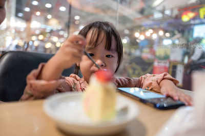 Cute girl eating ice cream with smart phone on table