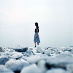 Surface level of woman standing on pebbles at beach against sky