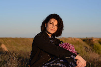 Portrait of young woman sitting on field against clear sky