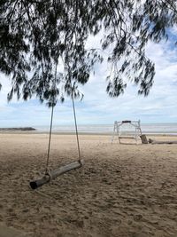 Empty swing on beach against sky