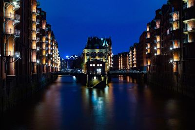 Illuminated canal amidst buildings against sky at night