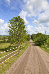 Road amidst trees on field against sky