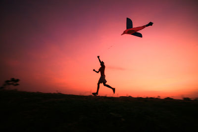 Boy flying kite against sky during sunset