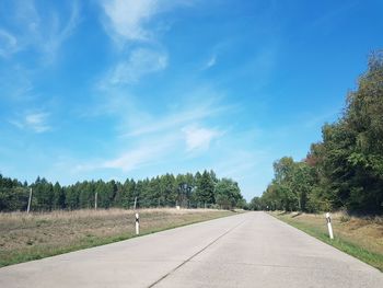 Empty footpath amidst trees against blue sky