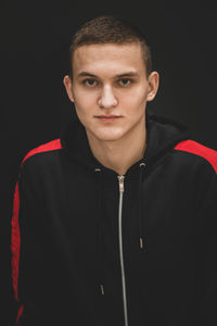 Portrait of young man standing against black background