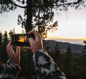 Man photographing with mobile phone against sky